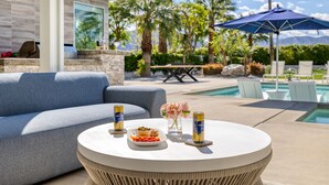 A poolside area with a round table, a sofa, and a patio umbrella.