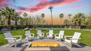 A fire pit with white chairs arranged around it, set in a landscaped area with palm trees and a pool in the background. - Private Pool + Spa + Pickleball Court + Fire Pit • Near La Quinta | Polo Villa 4 (La Quinta)