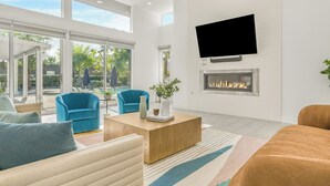 A modern living room with a fireplace, a flat-screen TV, and large windows. - Private Pool + Spa + Pickleball Court + Fire Pit • Near La Quinta | Polo Villa 4 (La Quinta)