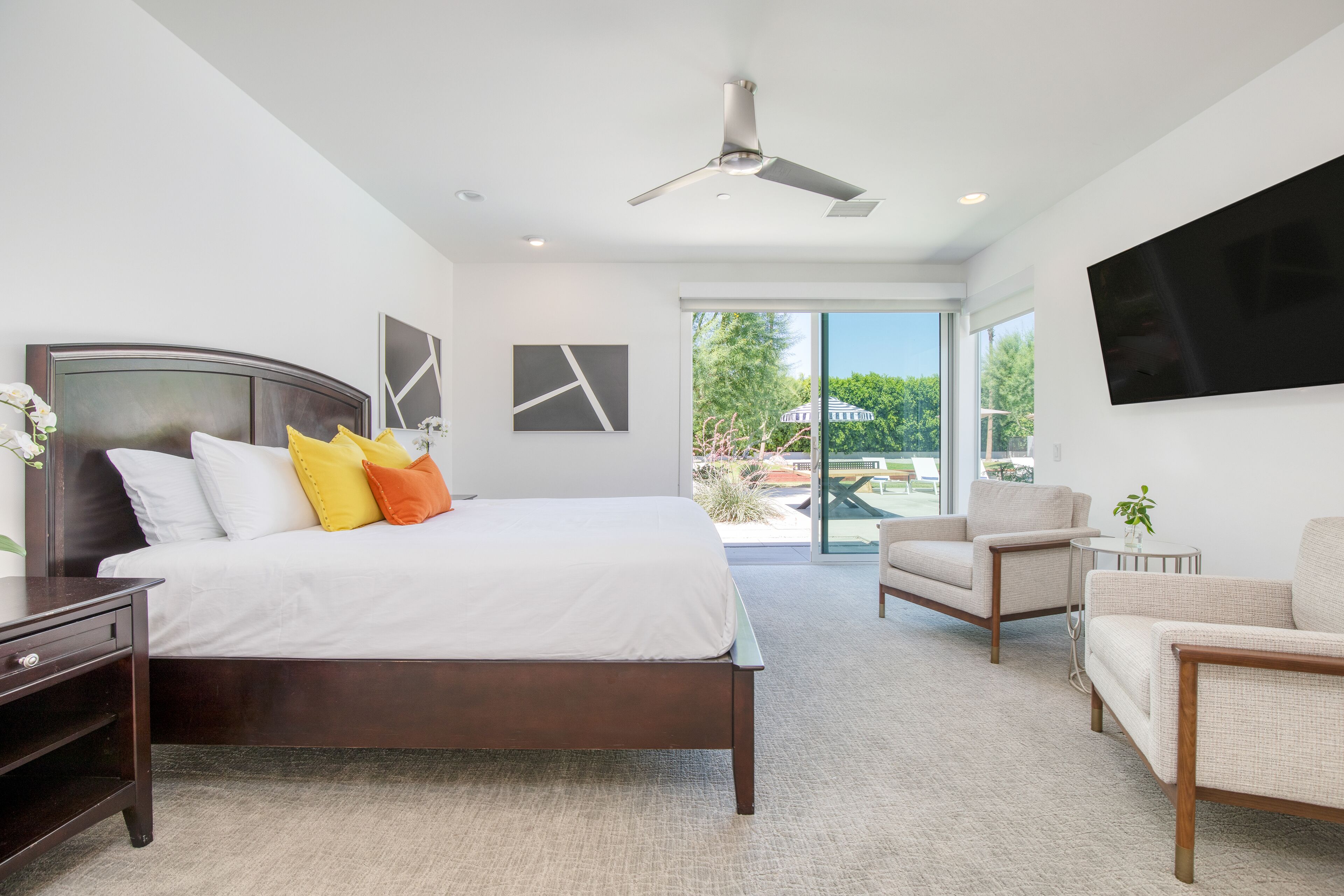 Un dormitorio moderno con una cama grande, un ventilador de techo y vistas al exterior a través de un ventanal corredero.