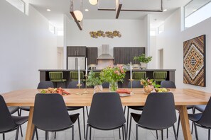 A modern dining area with a wooden table, black chairs, and a kitchen in the background.