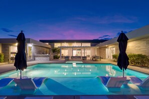 A swimming pool with lounge chairs and umbrellas, surrounded by a building with a stone facade and a glass door entrance. - Sleeps 16 • Private Pool + Spa + Putting Green • Near La Quinta | Polo Villa 10 (La Quinta)