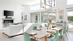 Ein modernes Wohnzimmer mit Kamin, einem Essbereich mit Holztisch und grünen Stühlen sowie einem großen Fenster mit Blick ins Freie.
