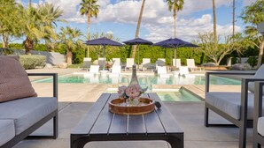 A poolside area with lounge chairs, umbrellas, and a table with a bottle and flowers.