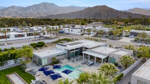 A modern resort with multiple buildings, a swimming pool with umbrellas, and palm trees.