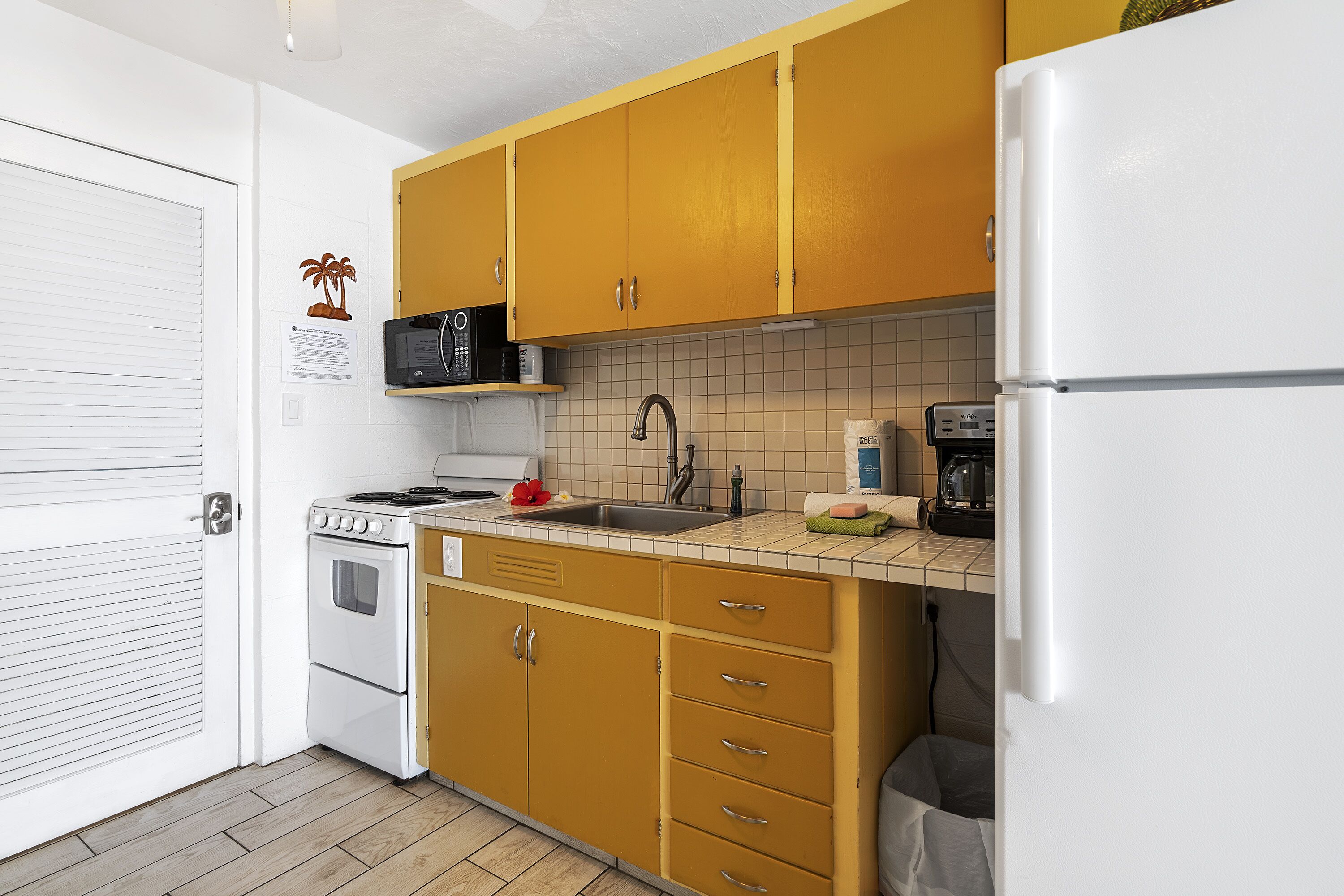 A compact kitchen with a white refrigerator, a stove, a microwave, and a sink.