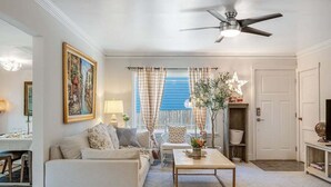 A living room with a sofa, coffee table, and a ceiling fan. There is a window with curtains and a door in the background. - Perch - Brygger Cottage: Magnolia rambler & pet-friendly (Seattle)