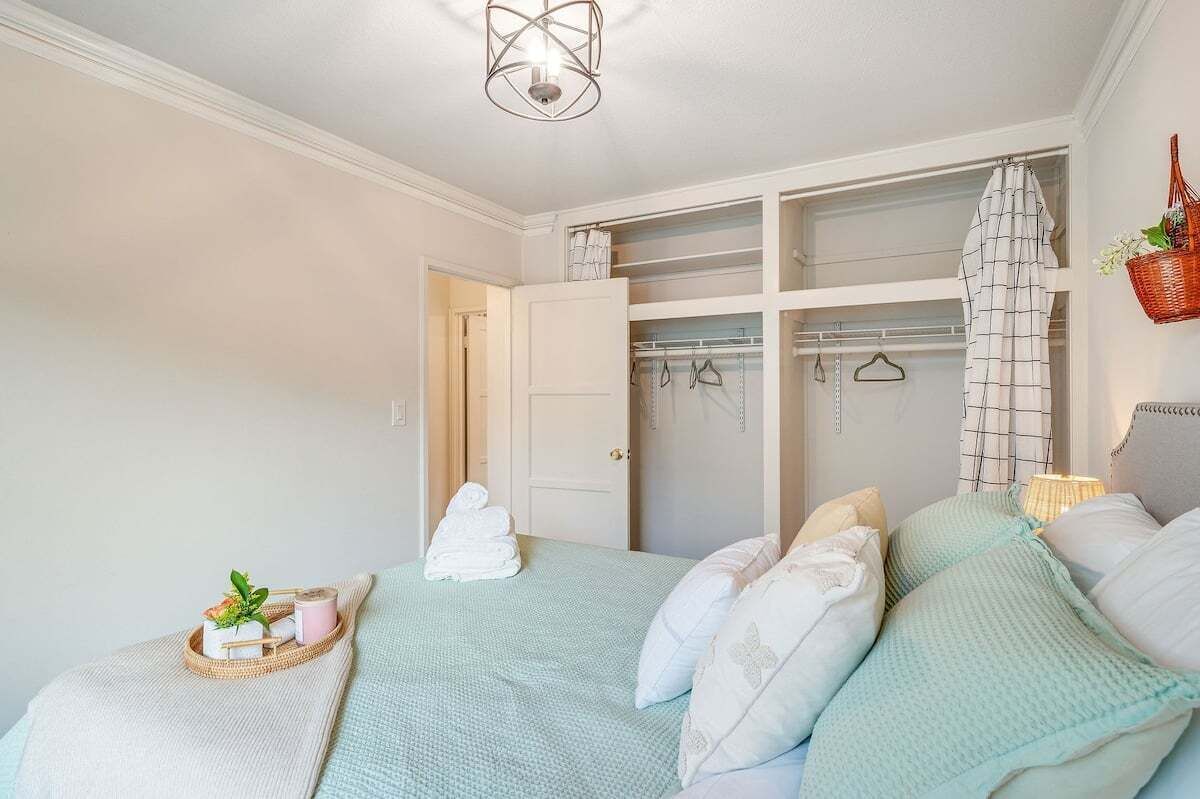 A bedroom with a bed, a bedside table with a tray, a closet with hanging clothes, and a basket on the wall.