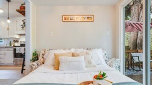 A bedroom with a bed, a bedside table with a tray of toiletries, and a view of the outside. - Perch - Brygger Cottage: Magnolia rambler & pet-friendly (Seattle)