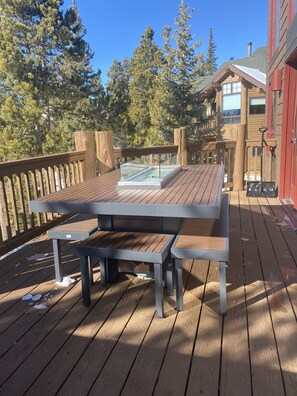 Eine Holzterrasse mit langem Tisch und Bänken, umgeben von einem Hollerdzaun und Bäumen.