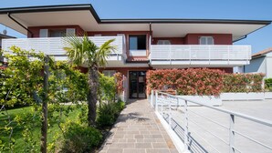 Ein zweistöckiges Gebäude mit Balkon, Kiesweg und üppiger Bepflanzung.