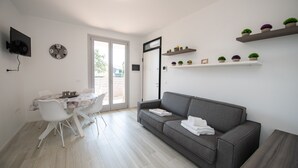 Ein modernes Wohnzimmer mit grauem Sofa, einem Esstisch mit Stühlen, einem flachbildfernseher an der Wand und einer Tür zu einem Außenbereich.