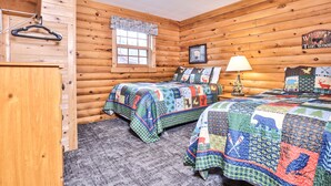 A cabin-style room with two beds, a wooden wall, a window, a lamp, and a welcome sign.