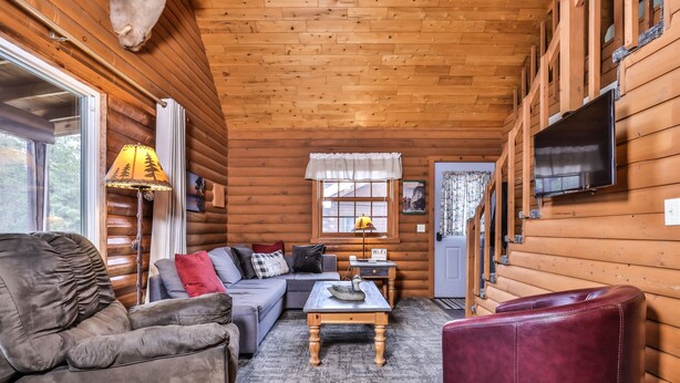 A cozy log cabin interior with a sofa, armchair, and a small coffee table.