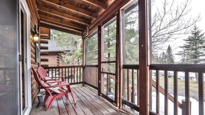 A wooden deck with red chairs, large windows, and a view of trees and a building in the background.