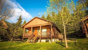 A wooden cabin with a porch, surrounded by trees and a clear sky. - Lakeside wilderness resort cabin with dock, fire pit, on-site store, bait shop! (Watersmeet)