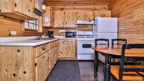 A wooden cabin-style kitchen with a dining area, including a stove, microwave, and refrigerator. - Lakeside wilderness resort cabin with dock, fire pit, on-site store, bait shop! (Watersmeet)