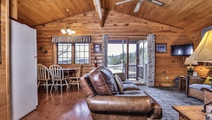 A log cabin interior with a leather sofa, wooden dining table, chairs, a TV, and a fireplace. - Lakeside wilderness resort cabin with dock, fire pit, on-site store, bait shop! (Watersmeet)