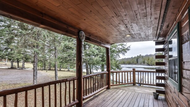 A wooden deck with a railing overlooking a river and forested area. - Lakeside wilderness resort cabin with dock, fire pit, on-site store, bait shop! (Watersmeet)