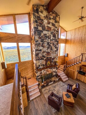 A spacious living area with a stone fireplace, wooden staircase, and large windows offering a view of the landscape. - Large cabin with amazing views, mountains, sunsets, and wildlife.
(Pinedale)