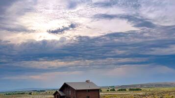 A wooden cabin in a grassy field with a cloudy sky.