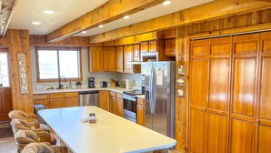 A spacious kitchen with wooden cabinets, a large island with stools, and a stone-tiled floor. - Large cabin with amazing views, mountains, sunsets, and wildlife.
 (Pinedale)