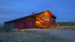 A log cabin with a red garage door, a porch with a railing, and a large window on the front. - Large cabin with amazing views, mountains, sunsets, and wildlife.
 (Pinedale)