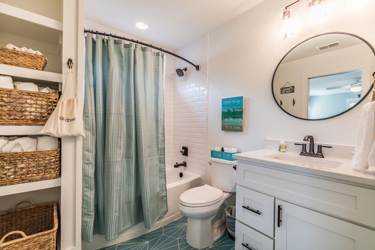 A bathroom with a bathtub, toilet, and a sink. There are wicker baskets on shelves and a towel hanging on the wall.