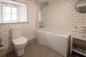A bathroom with white subway tiles, a toilet, a bathtub, and a window with a curtain.