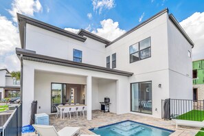 Una casa moderna de dos pisos con un patio, una piscina y una parrilla.