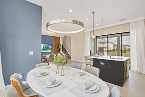 Un comedor moderno con una mesa redonda dispuesta para seis personas, una isla de cocina y vistas al exterior.