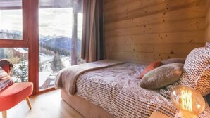 Una camera da letto con un'ampia finestra, un letto con coperta lavorata a maglia, una poltrona rossa e un lampadario.