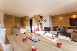 A cozy cabin interior with a wooden dining table set for four, a staircase, a fireplace, and a living area with a sofa and a couch. - 50m from resort center, 9th floor, view valley, balcony, fireplace or stove, tv, ski locker, 59m² (Les Arcs)