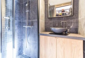 A modern bathroom with a glass-enclosed shower, a large sink with a vessel basin, and a mirror above the sink.