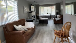 Ein modernes Wohnzimmer mit einem braunen Ledersofa, einem Holzstuhl, einem Couchtisch und einem Fernseher auf einem Schrank.