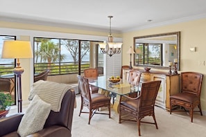 A dining area with a glass table, leather chairs, a chandelier, and a large mirror.