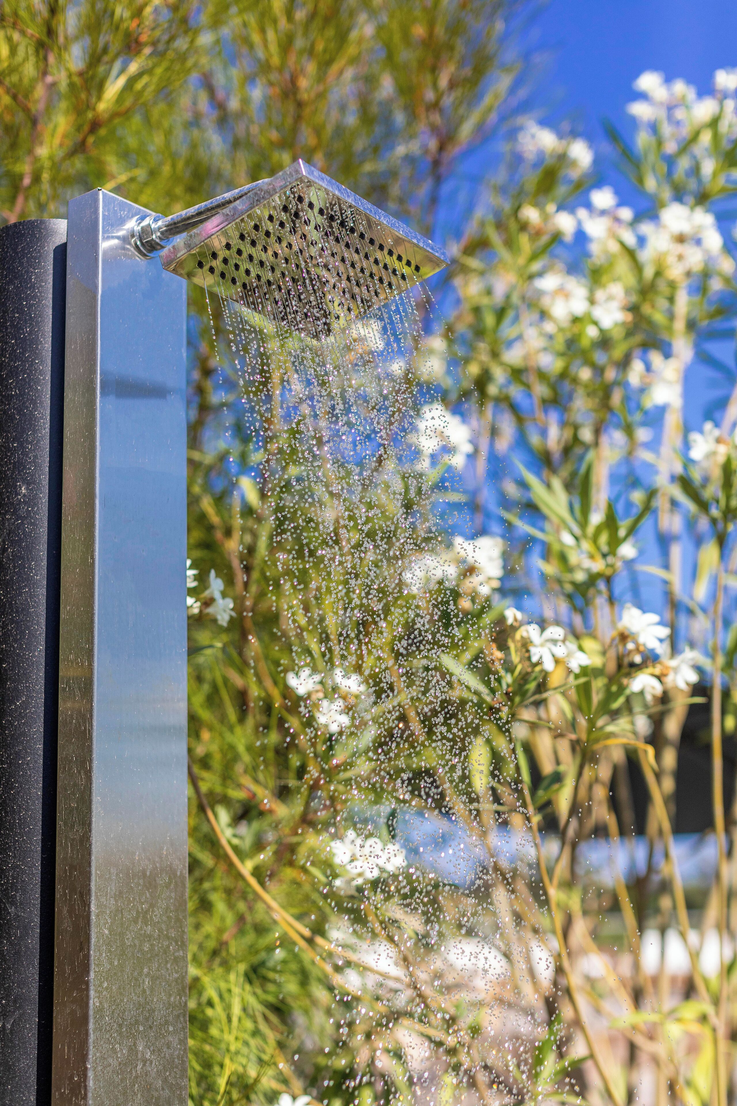 Une pomme de douche moderne d’où jaillit l’eau, entourée de verdure et de fleurs.
