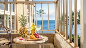 A balcony with a table set with a pineapple, grapes, a bottle of wine, and a flower.