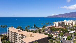 A coastal hotel with multiple balconies overlooking the sea, a parking area, and a view of the ocean.