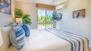 A bedroom with a bed, a TV, a window, and a plant.