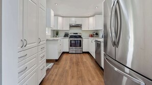 Une cuisine moderne avec des meubles blancs, des appareils en acier inoxydable et un plancher en bois.