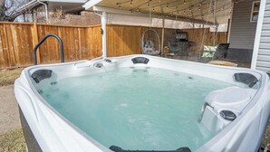 Un jacuzzi dans un jardin, avec une clôture en bois, un fauteuil suspendu et un barbecue.