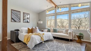 Une chambre avec un lit, un canapé, une fenêtre donnant sur un beau paysage et deux œuvres d’art murales.
