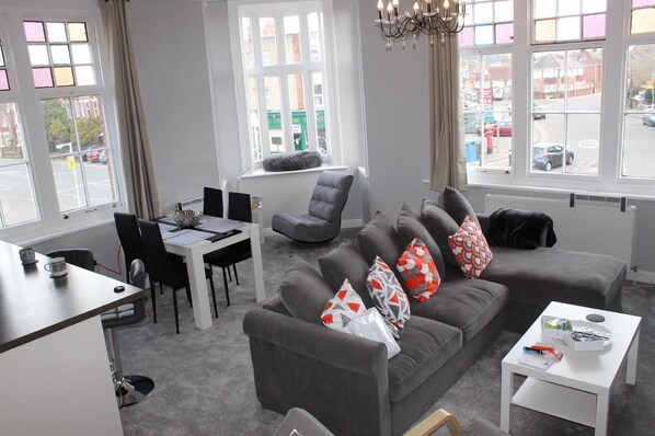 A modern living room with a grey sofa, a dining table, and a white coffee table.
