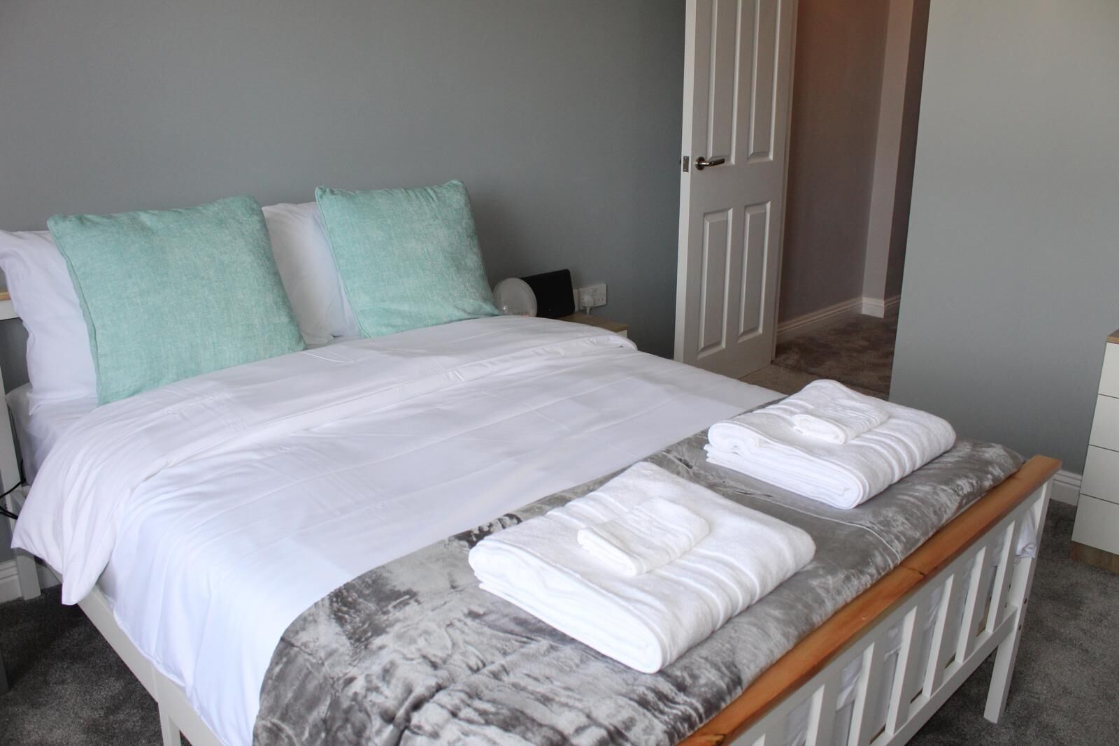 Cama bem arrumada com roupa de cama branca e duas almofadas verde-água, um edredom estampado com padrão de mármore e duas toalhas dobradas na cabeceira.