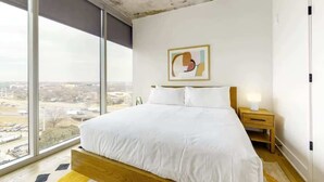 A bedroom with a large window, a bed, a nightstand, and a wall-mounted artwork. - Luxe Rainey St High Rise / Heated Pool / Gym / ATX (Austin)