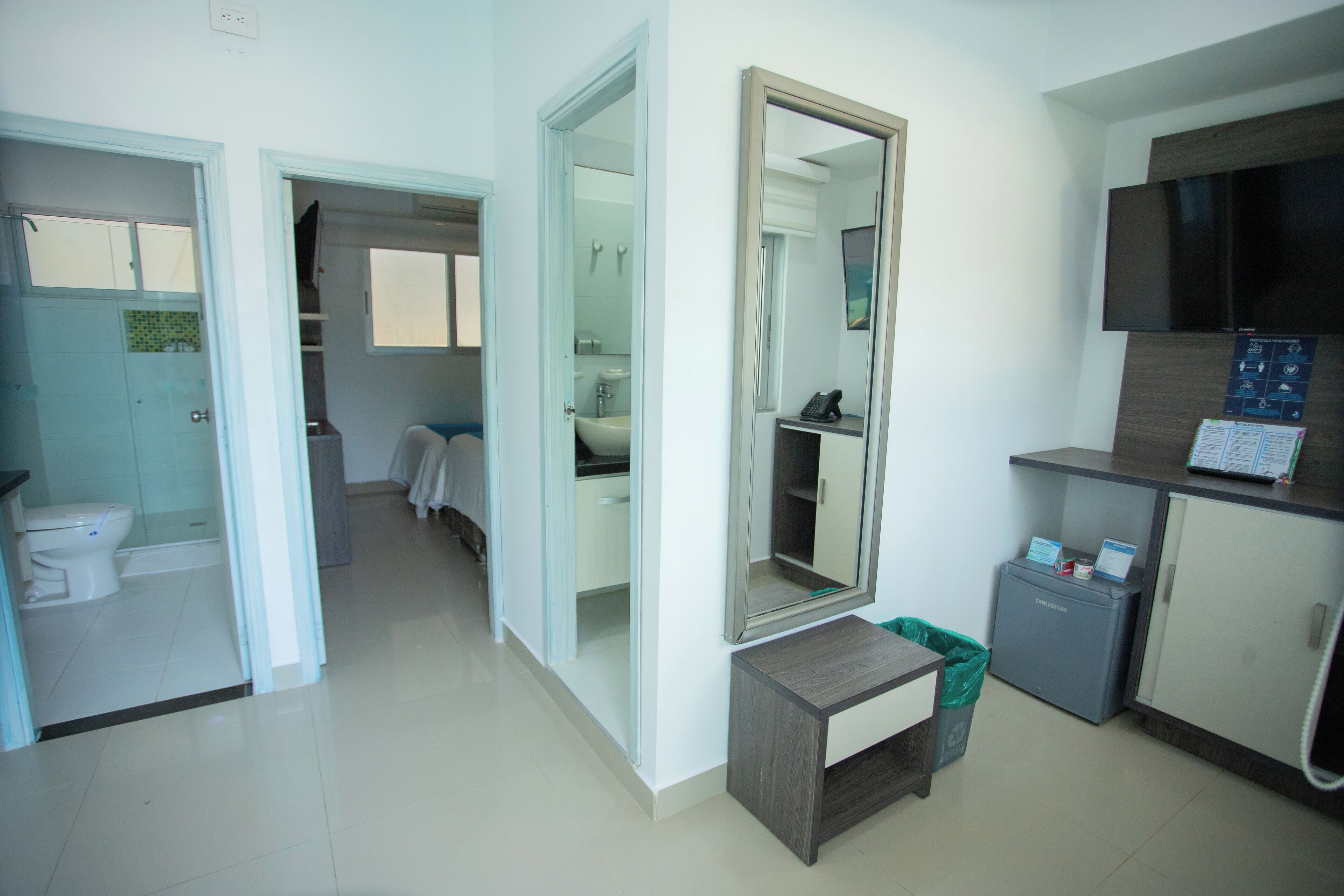 Una habitación de hotel con baño, espejo, escritorio y televisión.