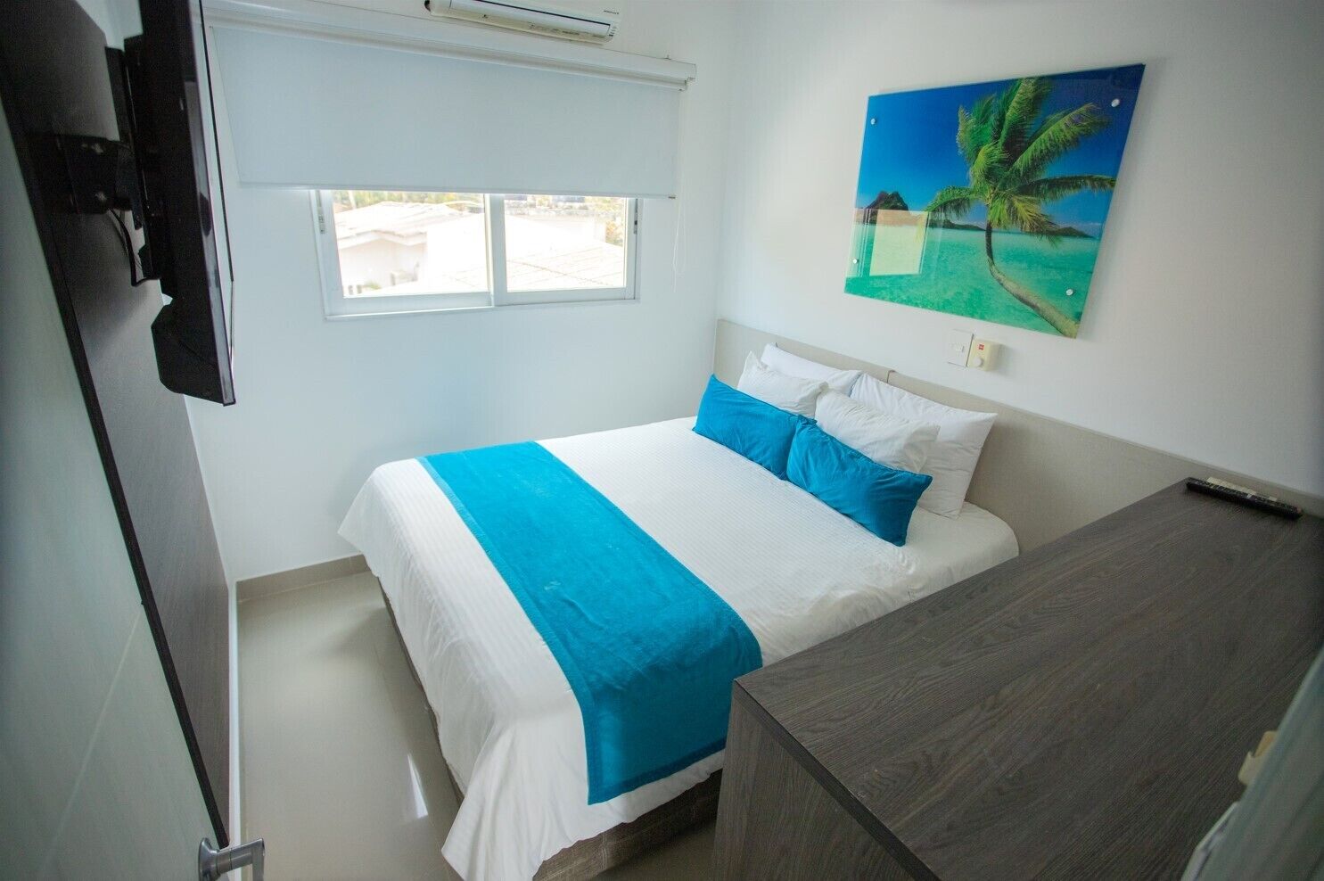 Una habitación de hotel con una cama, un cuadro de una playa y una ventana que da a edificios.