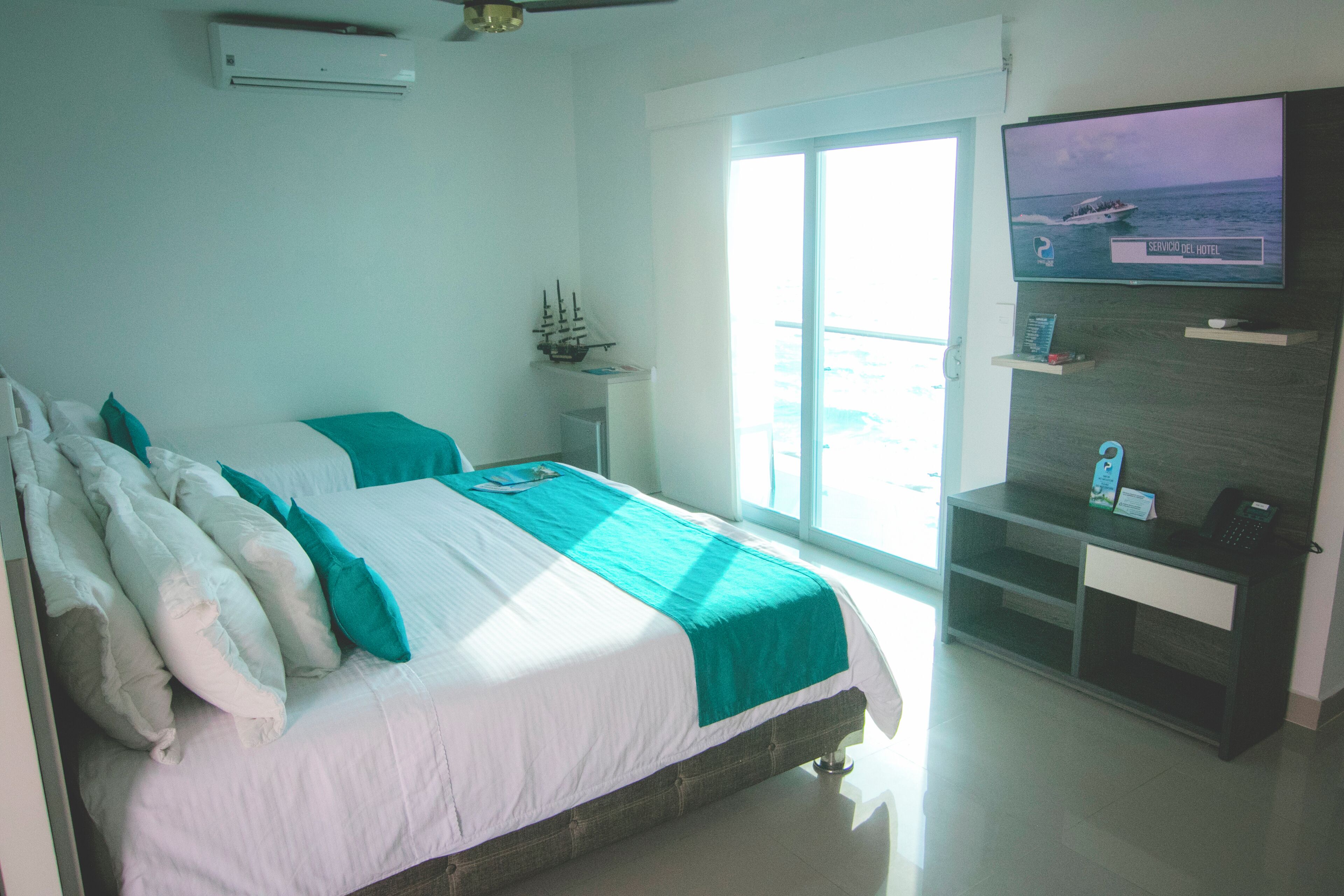 A hotel room with a bed, a desk, a television, and a window with a view of the sea.