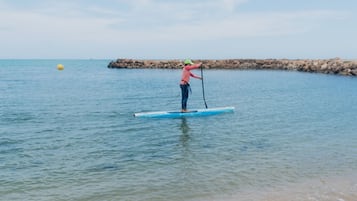 A person paddleboarding on a calm body of water with a rocky shoreline in the background.